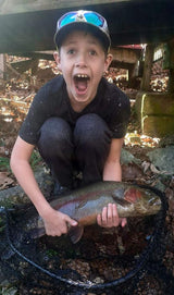 A young boy holding a trout he caught above a net at Dry Run Creek in Arkansas.