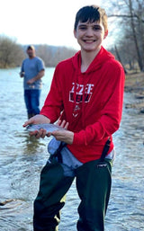 A young boy wearing wade pants while holding a trout in the Spring River in Arkansas.