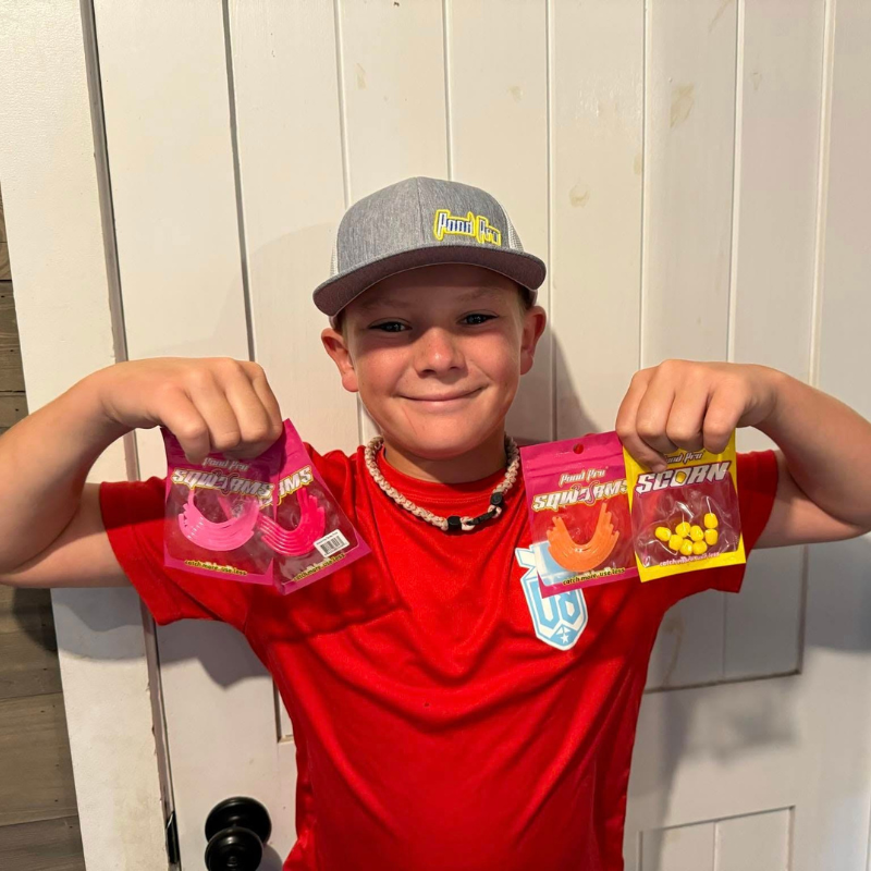 A young boy holding packages of Pond Pro Scorn + Sqworms while wearing a Pond Pro Hat in the color gray.
