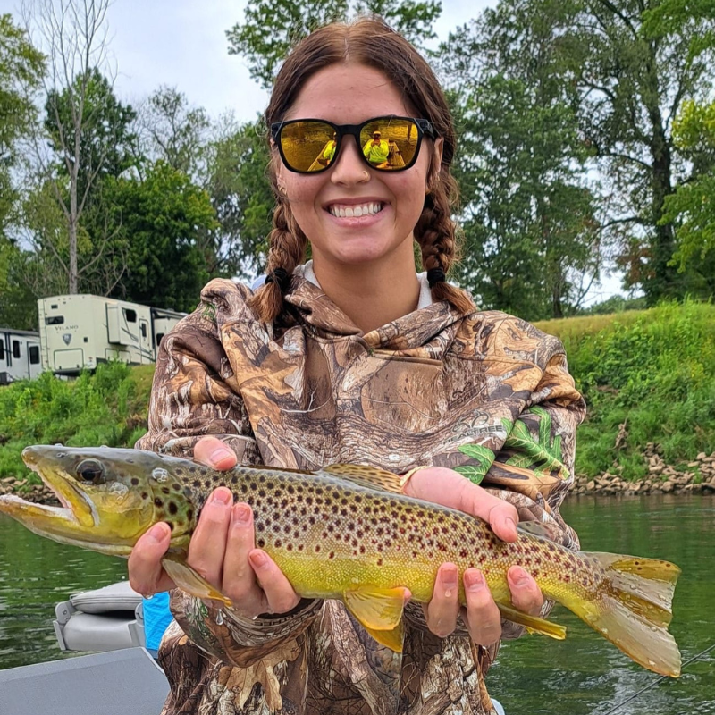 Young girl holding a trout she caught while fishing. River in the background.