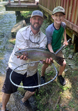 Pond Pro Guide, Tim Shannon, holding a large trout, standing next to a young boy holding a net at Dry Run Creek in Arkansas.
