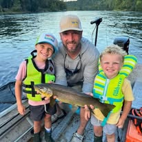 Pond Pro Guide, Tim Shannon, on a boat with two young boys, holding a large trout, on the White River in Arkansas.