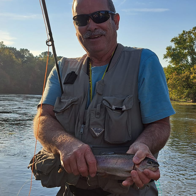 A man fly fishing while standing in river holding a fish while fishing with Pond Pro Tim Shannon