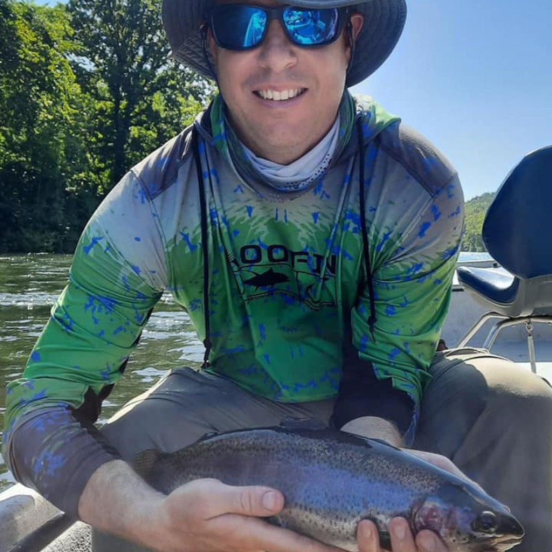 Man holding a fish on a boat with a green and blue shirt and sunglasses