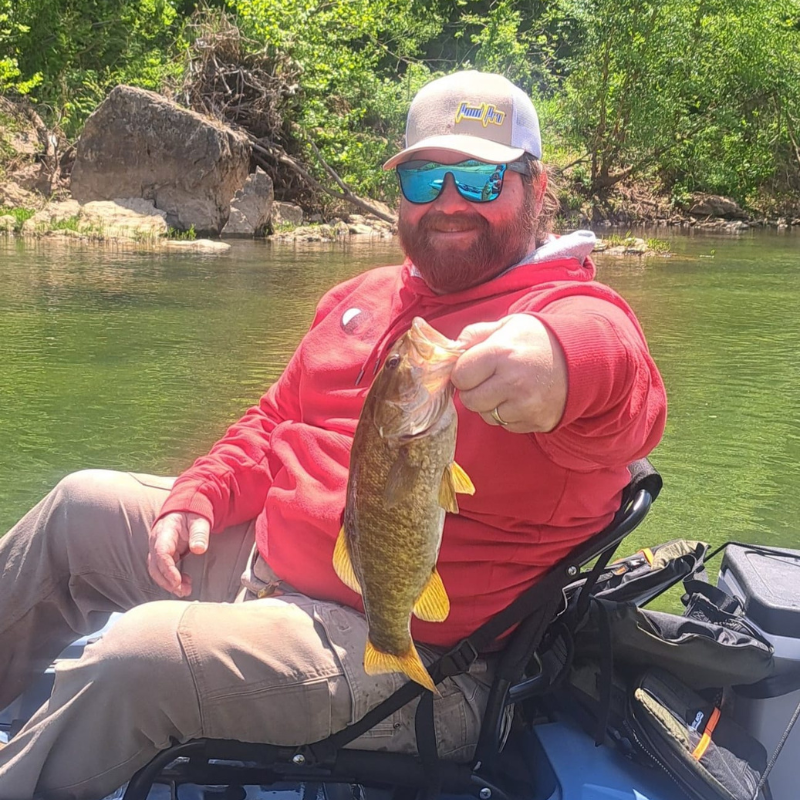 Guy holding a fish while kayaking in the river.