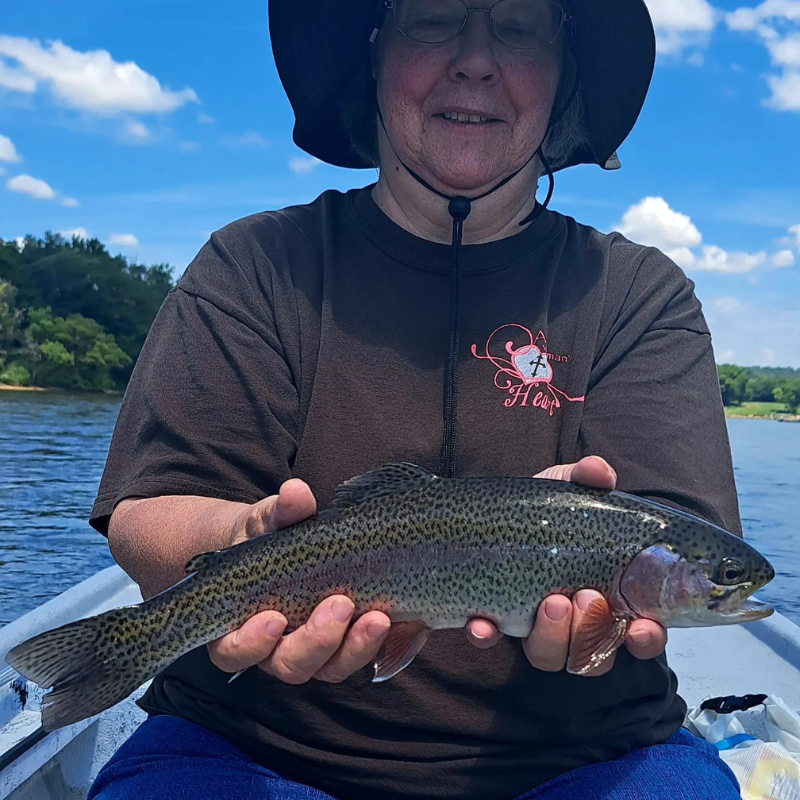 Person holding a rainbow trout on a boat with a scenic background