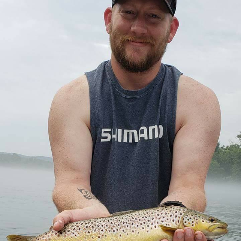 Man holding a trout while standing in foggy river.