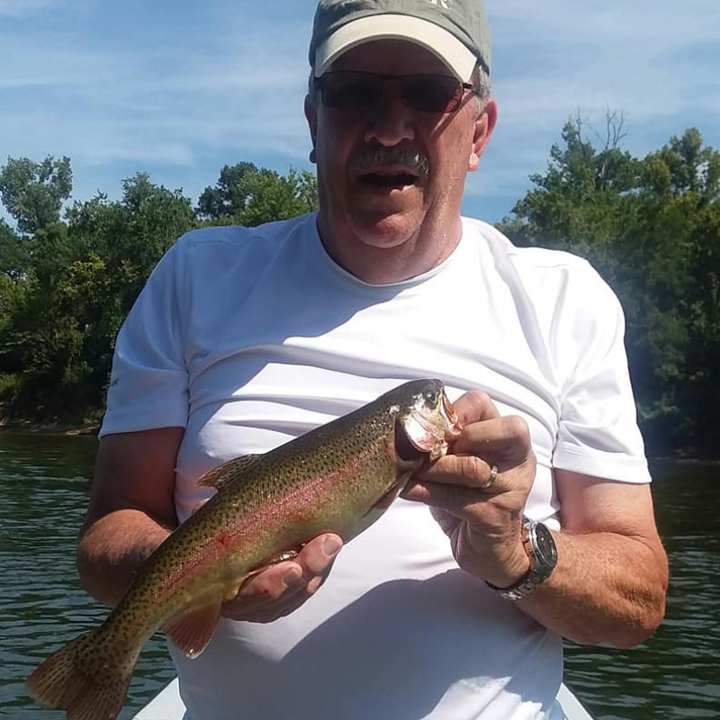 Man holding trout while fishing on a boat.
