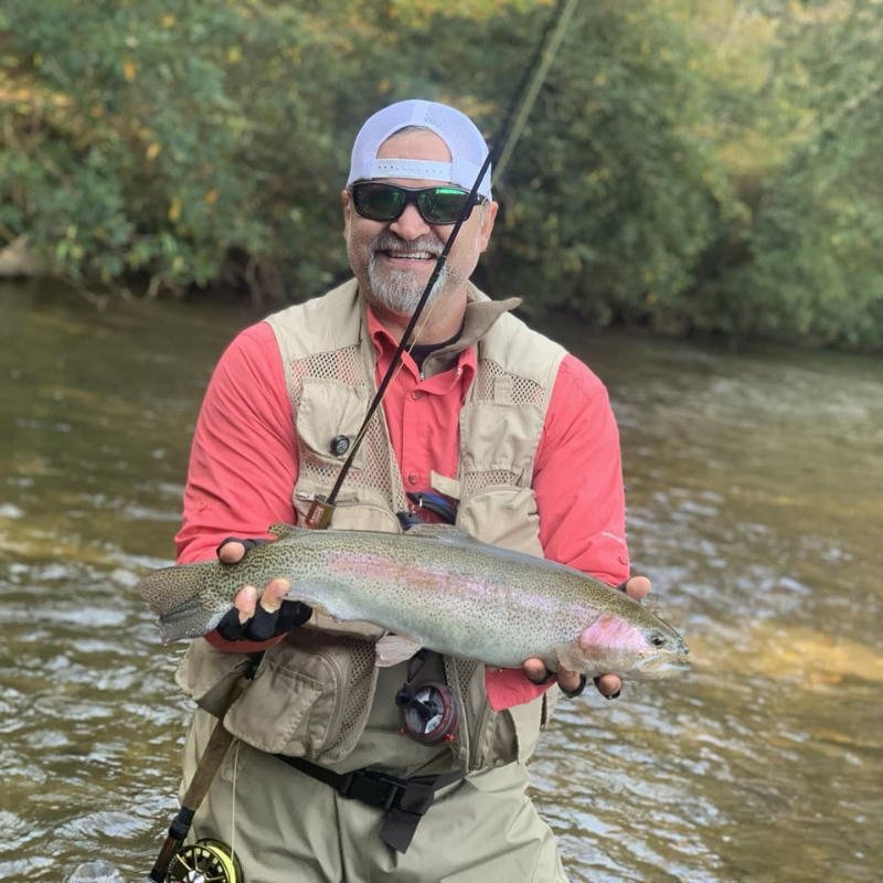 Man holding a fish by a river with fishing gear