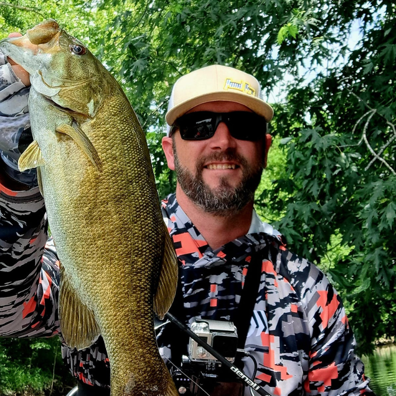 Man holding a large fish outdoors with greenery in the background